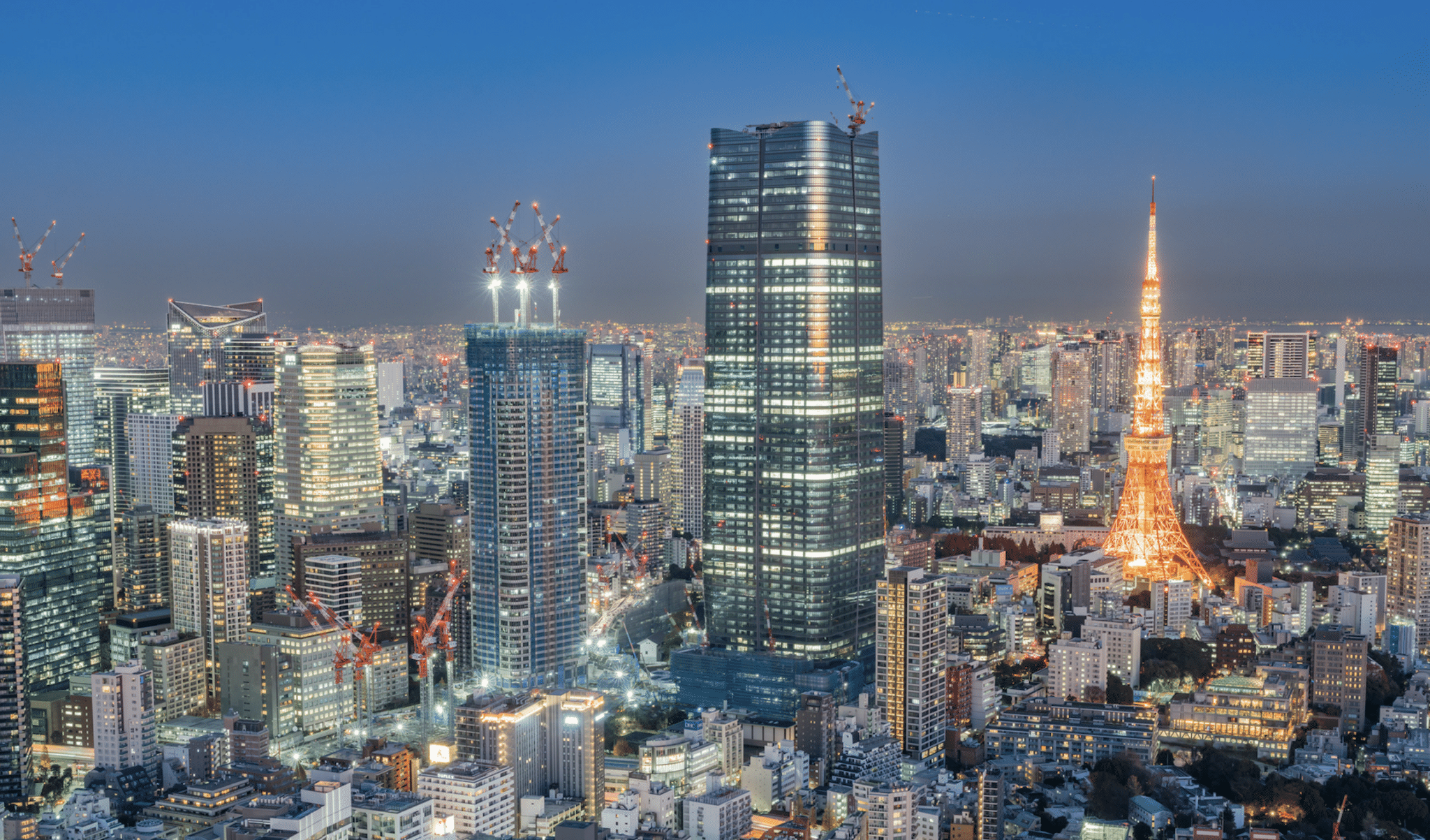 Azabudai Hills Mori JP Tower hovers above a Tokyo skyline at dusk, with lights twinkling. Nearby is Tokyo Tower.
